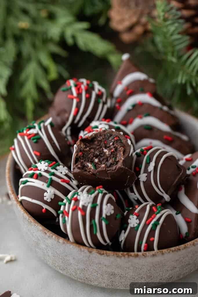Bowl of chocolate Christmas tree cake truffles topped with white drizzle and sprinkles, with one truffle sliced open.