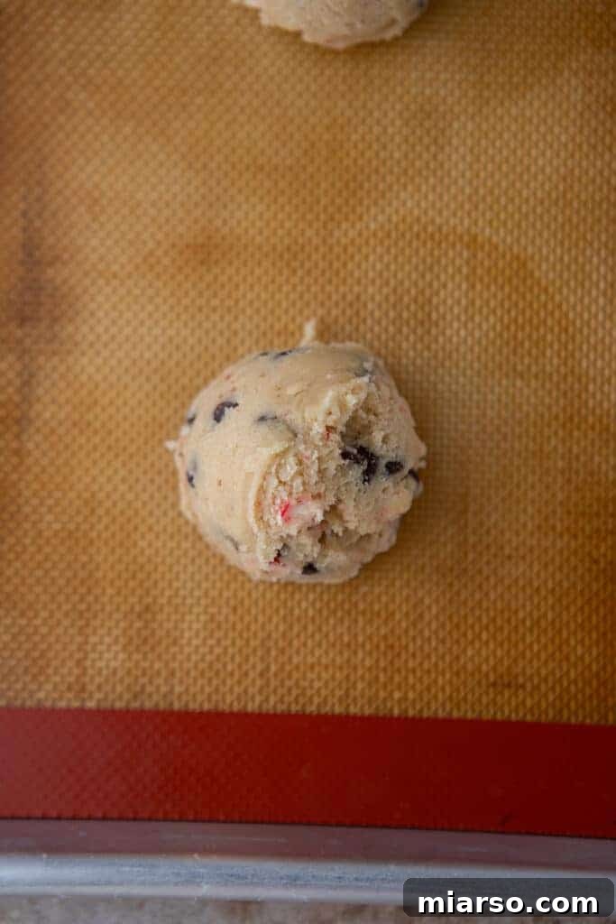 Perfectly scooped raw cookie dough balls, evenly spaced on a parchment-lined baking sheet, ready for the oven.