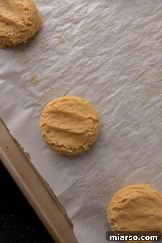 Pressed cookie dough balls neatly arranged on a parchment-lined baking sheet, prepared for the oven.