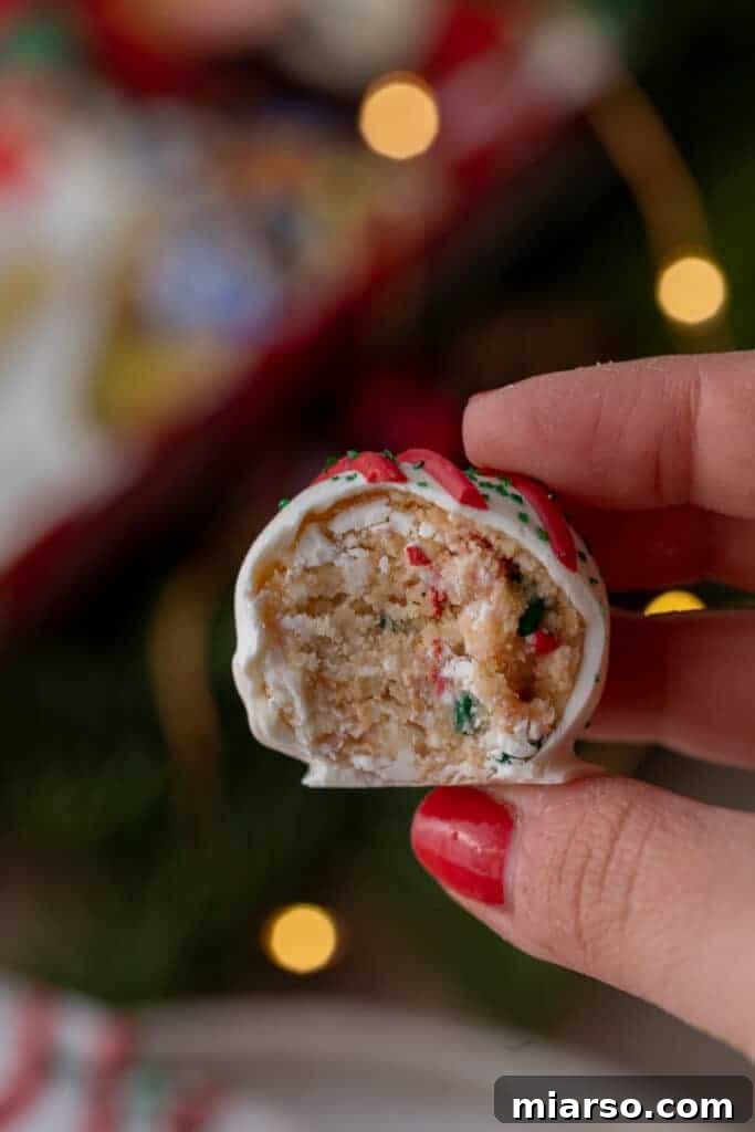 Easy No-Bake Little Debbie Christmas Tree Truffles 5 A hand holds up a Little Debbie Christmas Tree Cake Truffle, split in half to reveal the soft, sprinkle-flecked vanilla cake interior.