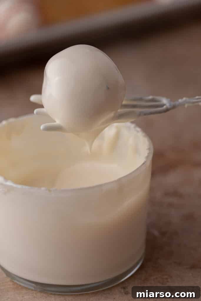 Easy No-Bake Little Debbie Christmas Tree Truffles 8 A cake ball being carefully dipped into a bowl of melted white chocolate, illustrating the coating process.