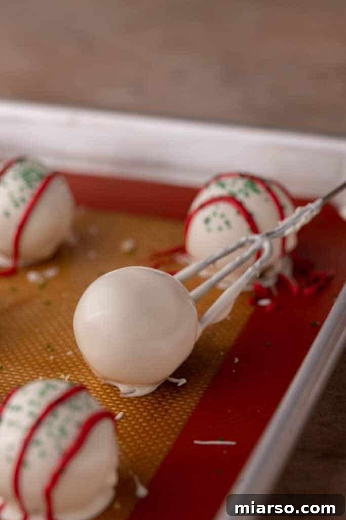 Easy No-Bake Little Debbie Christmas Tree Truffles 9 A white chocolate-dipped cake ball being carefully placed onto a parchment-lined baking sheet.