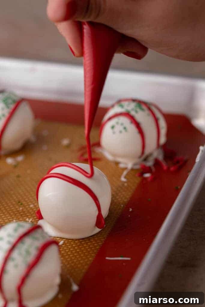 Easy No-Bake Little Debbie Christmas Tree Truffles 10 Melted red candy melts being drizzled in a festive pattern over a white chocolate-coated truffle.