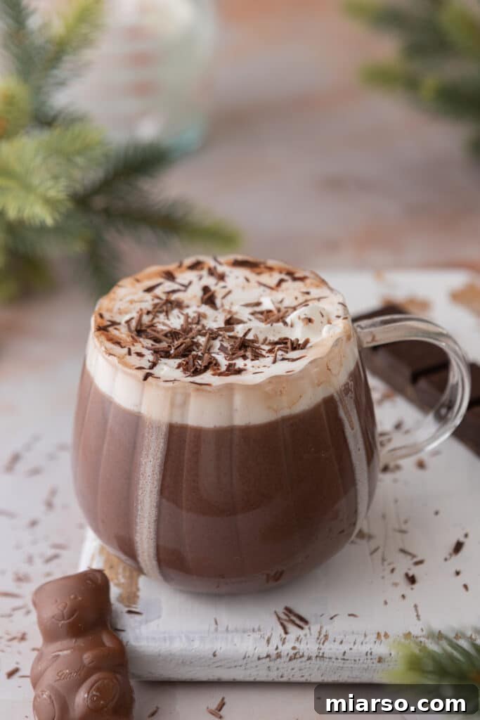 Angled overhead shot of a single serving of rich hot chocolate in a clear glass mug, topped with whipped cream.