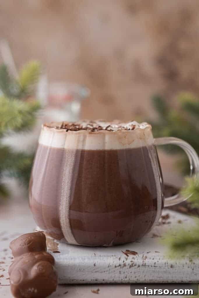 Side shot of a hot chocolate for one in a clear glass mug, topped with a frothy layer.