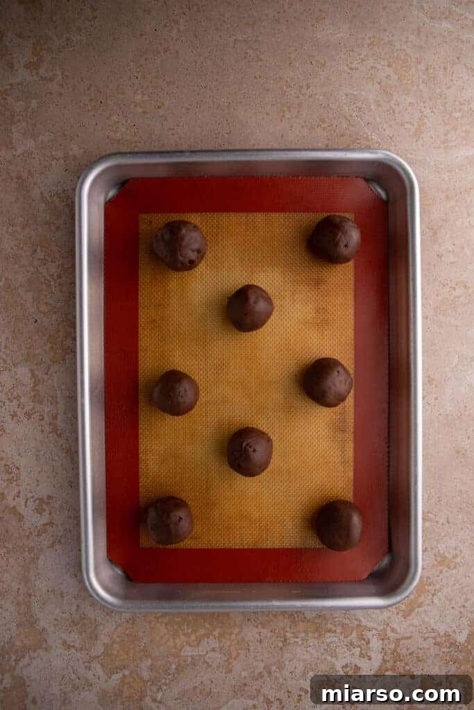 Chocolate cookie dough rolled into balls on a lined baking sheet.