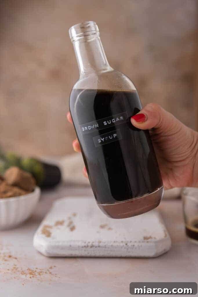 A hand reaching for a jar of freshly made brown sugar syrup, highlighting its homemade appeal.
