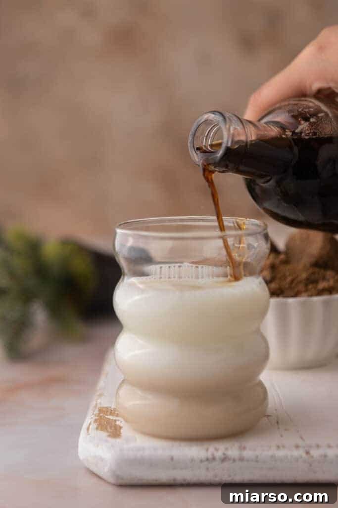 Freshly made brown sugar syrup being poured into a cup of coffee, ready to be enjoyed.