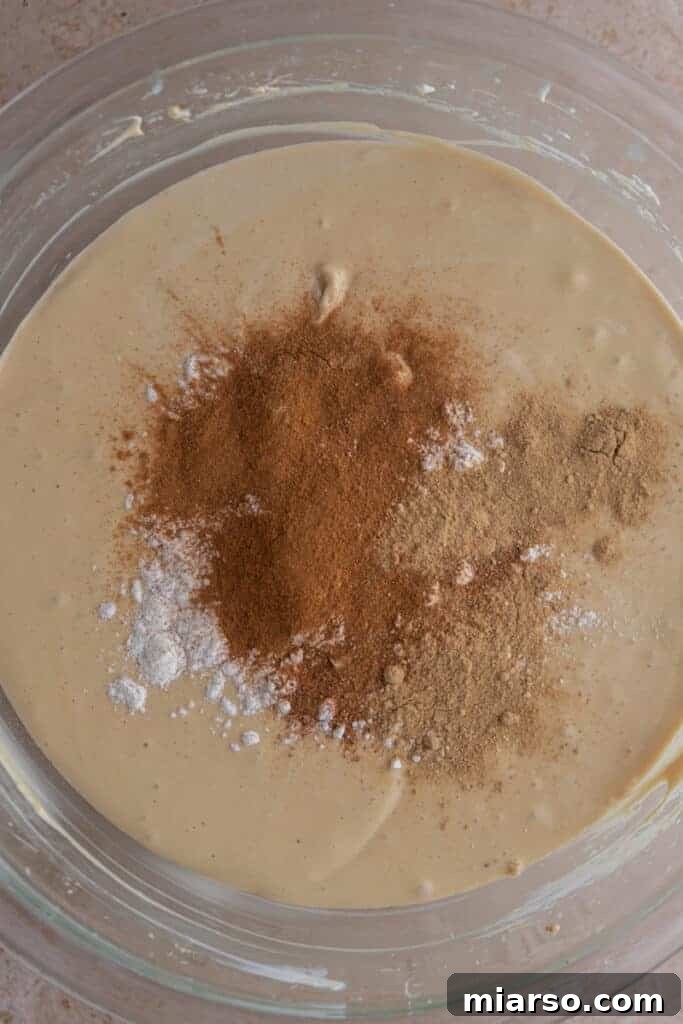 A colorful array of ground spices, including ginger, cinnamon, and nutmeg, on top of the cheesecake batter.