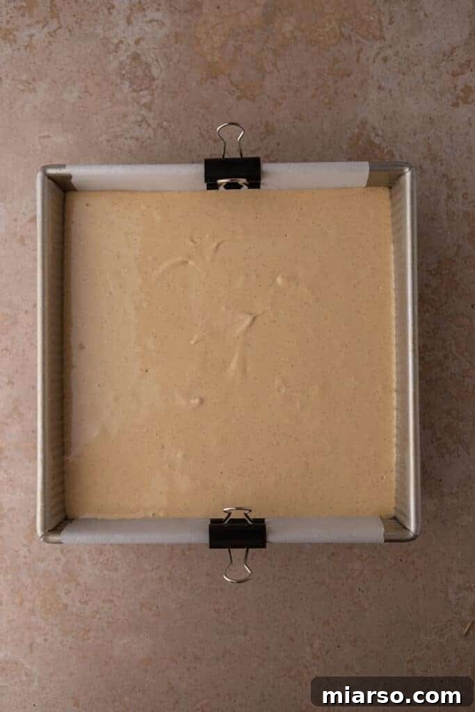 The unbaked gingerbread cheesecake batter, smooth and ready to be baked, sitting on the gingersnap crust in a pan.