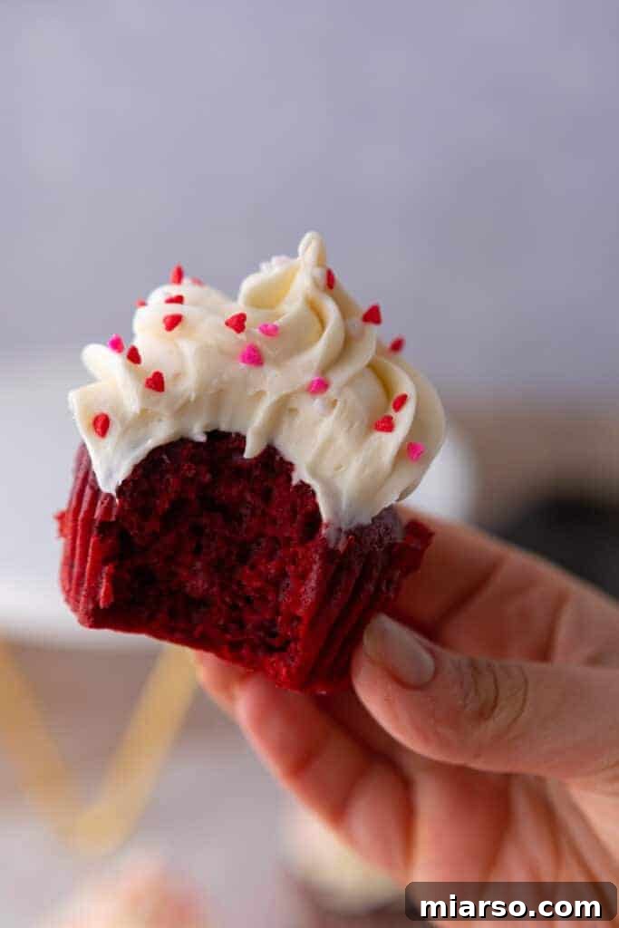 One of the small batch Red Velvet cupcakes, beautifully frosted and with a bite taken out, held up by a hand.