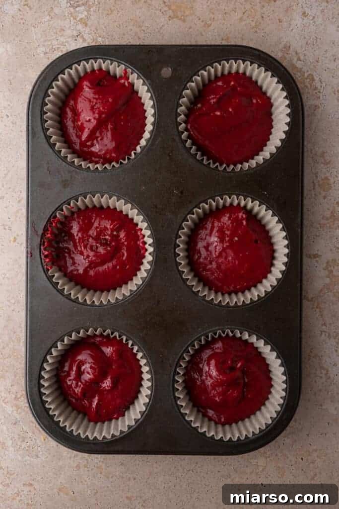 Raw red velvet batter in cupcake liners, placed in a muffin pan, ready for baking.