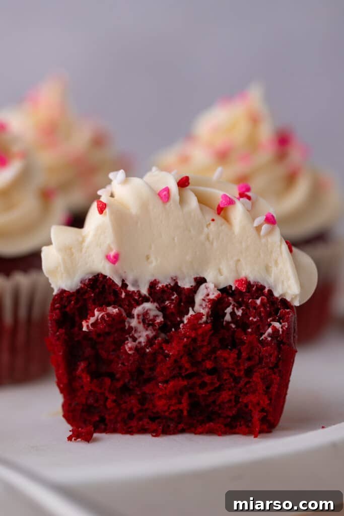 A small batch red velvet cupcake split in half, revealing its moist red interior and fluffy cream cheese frosting.