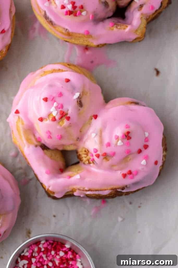 Valentines Sweetheart Cinnamon Buns Made Easy 11 A close-up view of a beautifully iced Valentine's Day heart-shaped cinnamon roll, showing off its generous pink frosting and festive sprinkles.