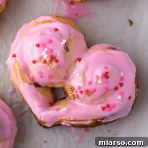 Close-up of a perfectly baked and decorated Valentine's Day heart-shaped cinnamon roll, glistening with pink icing and sprinkles.