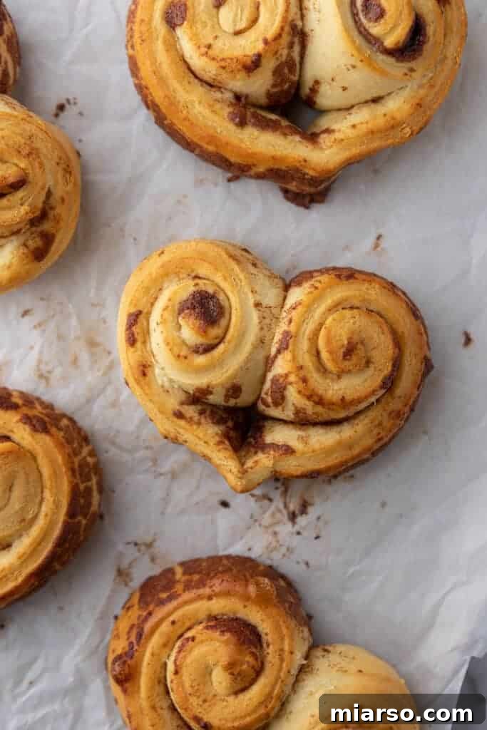 Valentines Sweetheart Cinnamon Buns Made Easy 10 A baking sheet filled with perfectly baked heart-shaped cinnamon rolls, golden brown and ready for frosting, resting on parchment paper.