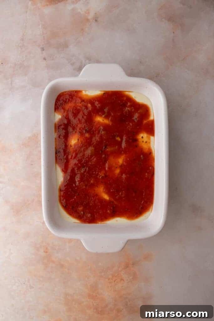 Rich marinara sauce layered over the cottage cheese base in a dish, preparing for cheese and toppings.