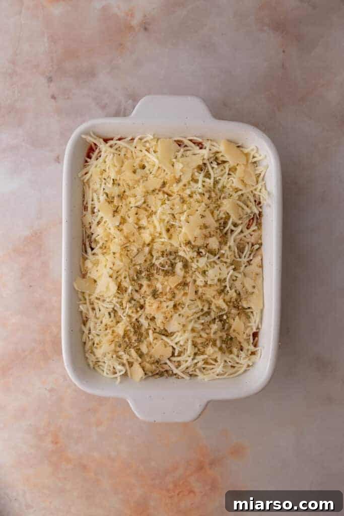 Generous shredded mozzarella and parmesan cheese sprinkled over marinara sauce, ready for pepperoni.