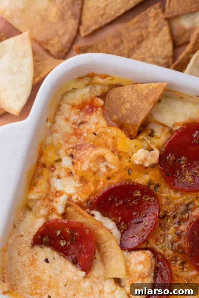 Close-up of the bubbly, delicious cottage cheese pizza bowl dip in a dish, with a chip scooping a portion.