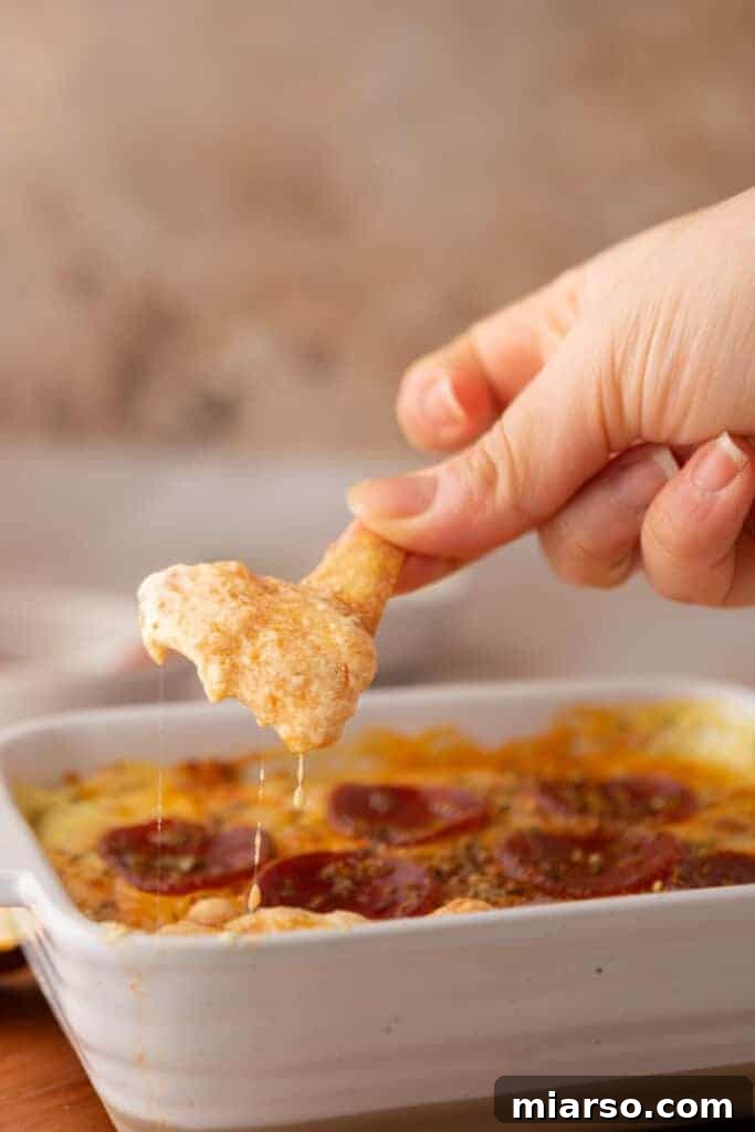 A hand holding a chip with a scoop of creamy cottage cheese pizza bowl dip, emphasizing its delicious and dippable nature.