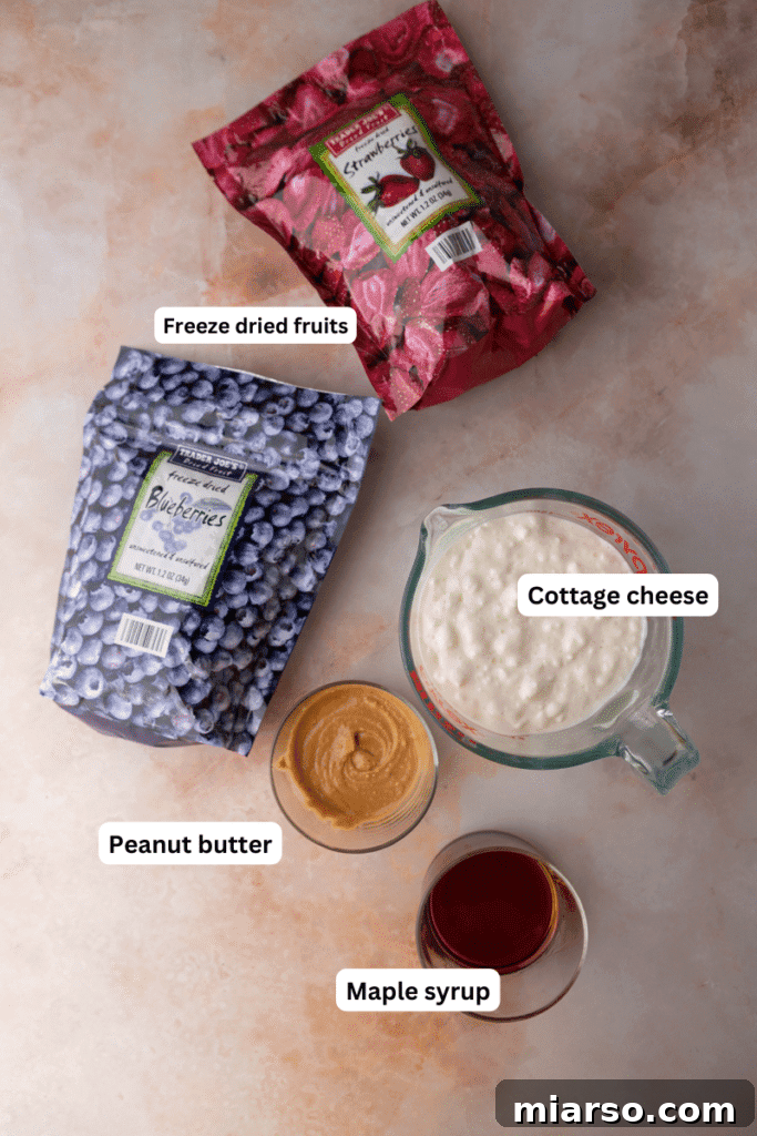 Protein Packed Cottage Cheese Freezer Bark 3 Carefully arranged ingredients for making frozen cottage cheese bark, including cottage cheese, maple syrup, peanut butter, and freeze-dried berries.