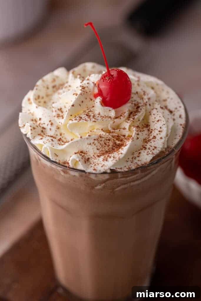 An angled overhead shot of a freshly made chocolate milkshake, garnished with whipped cream and chocolate shavings.