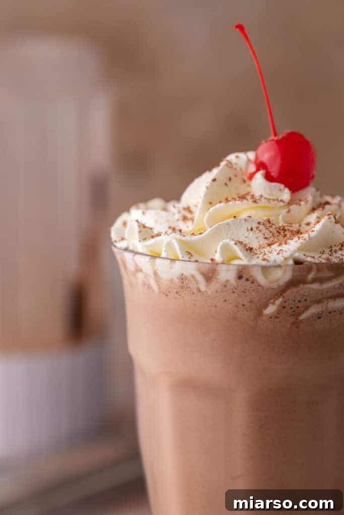 A close-up view of the top of a chocolate milkshake, showing the whipped cream and chocolate shavings.