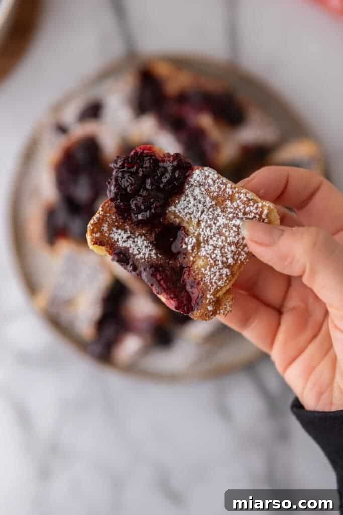 A hand holding a piece of golden-brown Hawaiian Roll French toast, perfectly cooked and ready to eat.