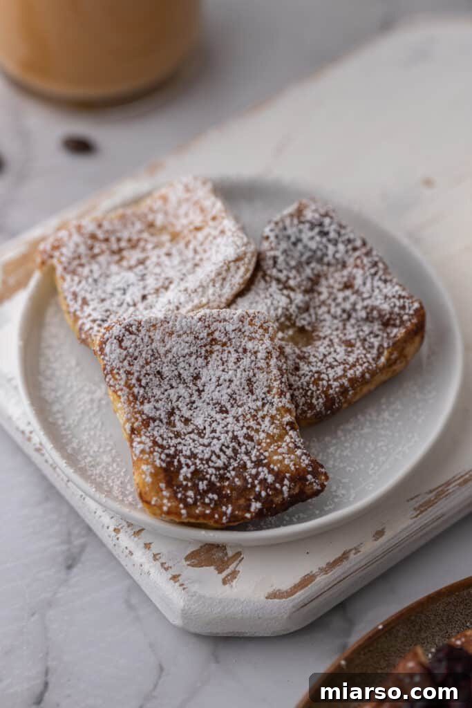 Three perfectly cooked Hawaiian roll French toast pieces artfully arranged on a white plate, ready to be enjoyed.