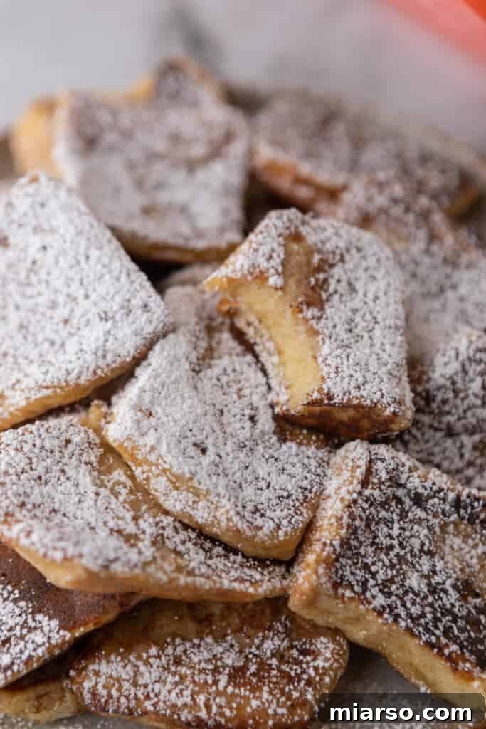 A stack of golden Hawaiian roll French toast pieces, lightly dusted with powdered sugar, ready to be served for breakfast.