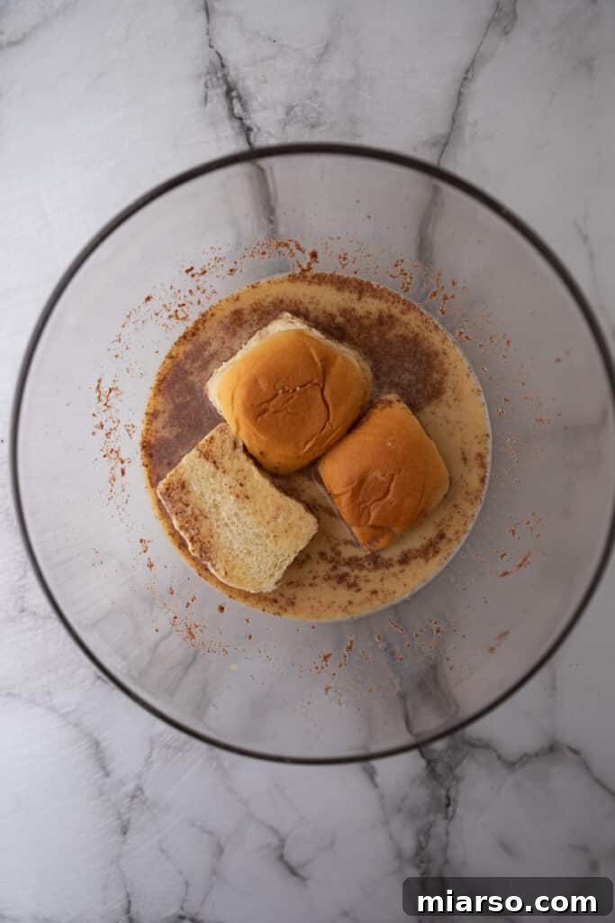 A King's Hawaiian roll half being carefully dipped into the French toast batter, ensuring an even coating.