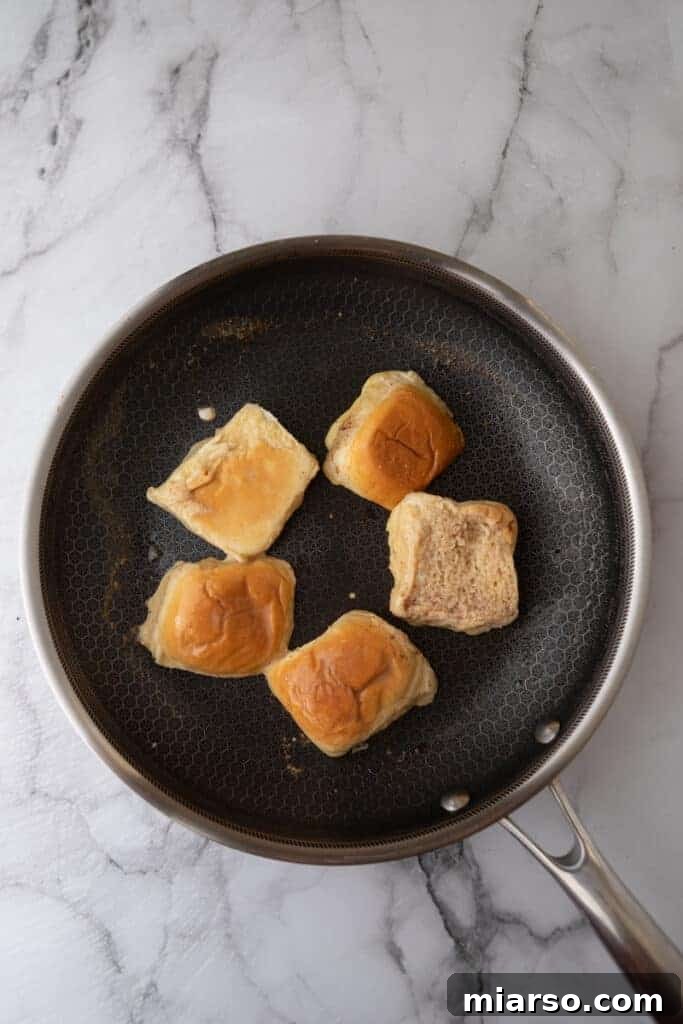 Perfectly battered Hawaiian roll halves sizzling on a hot skillet, beginning to turn golden brown.