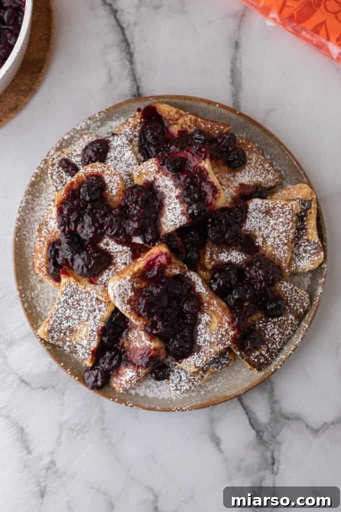 An overhead shot of Hawaiian roll French toast arranged artfully on a plate, garnished with fresh berries and a light dusting of powdered sugar.
