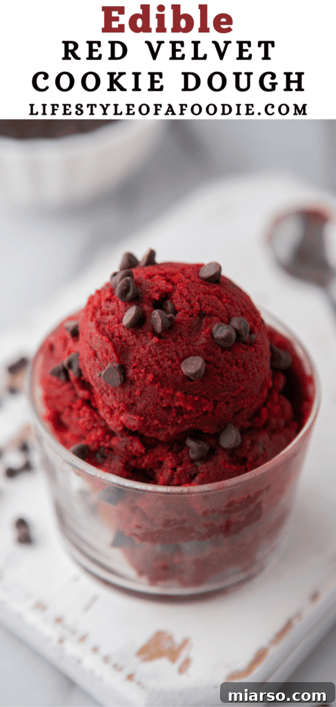 Vibrant red velvet cookie dough in a bowl, with a spoon taking a scoop.