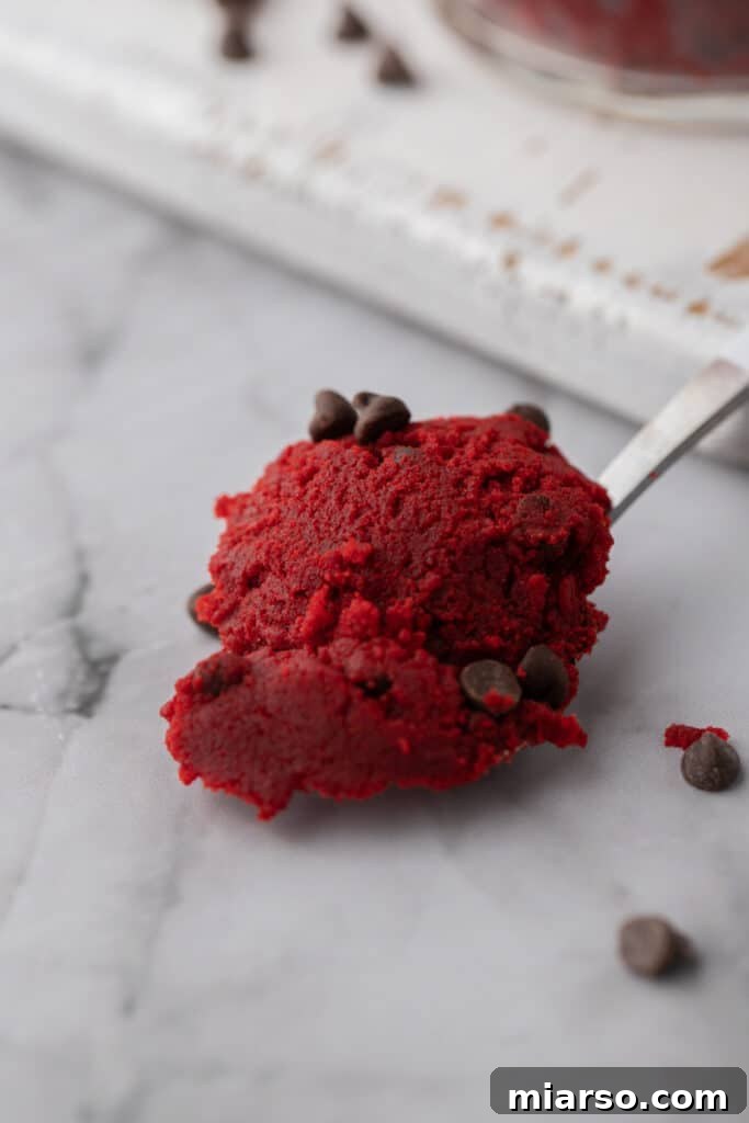 A spoonful of vibrant red velvet cookie dough, studded with chocolate chips, ready to be enjoyed.