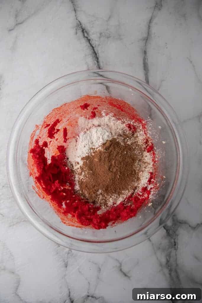 Wet ingredients, including red food coloring, mixed with dry ingredients in a bowl, forming a rich red dough.