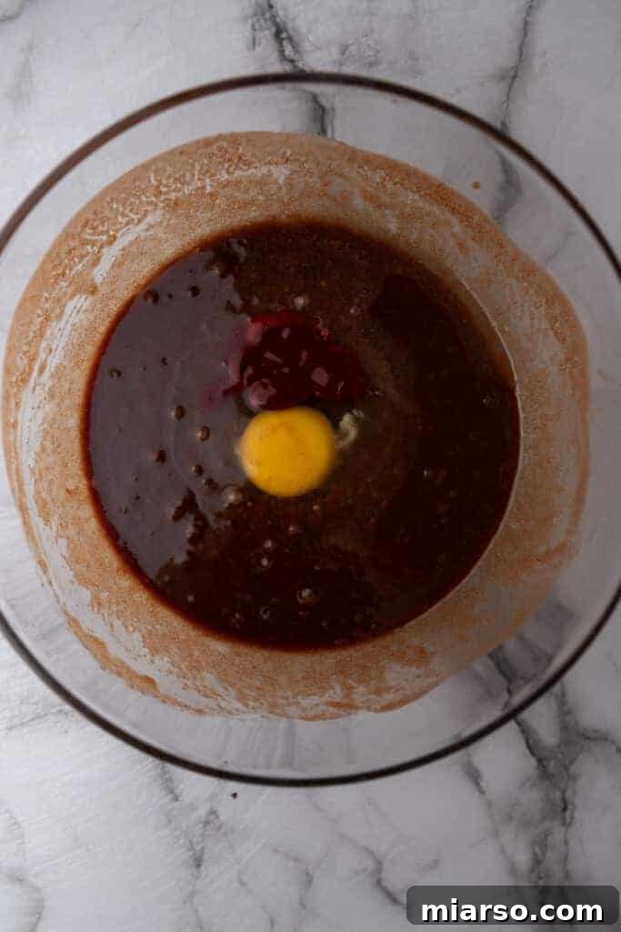 Further mixing of wet ingredients for red velvet brownies, ensuring all components are well combined.