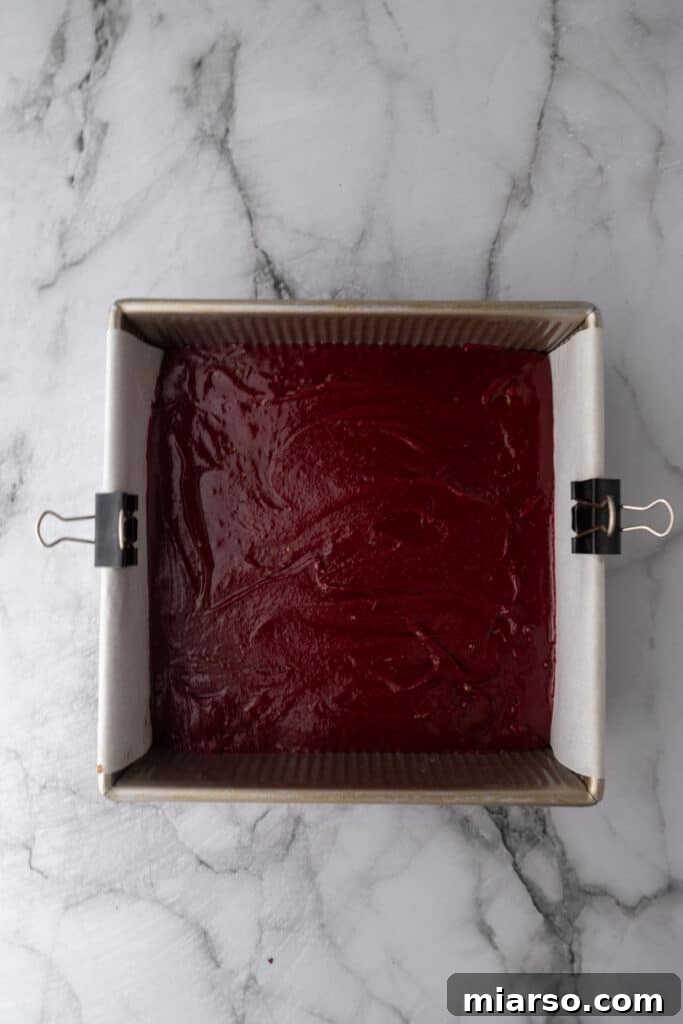 Red velvet brownie batter spread evenly in a prepared baking pan, ready for the oven.