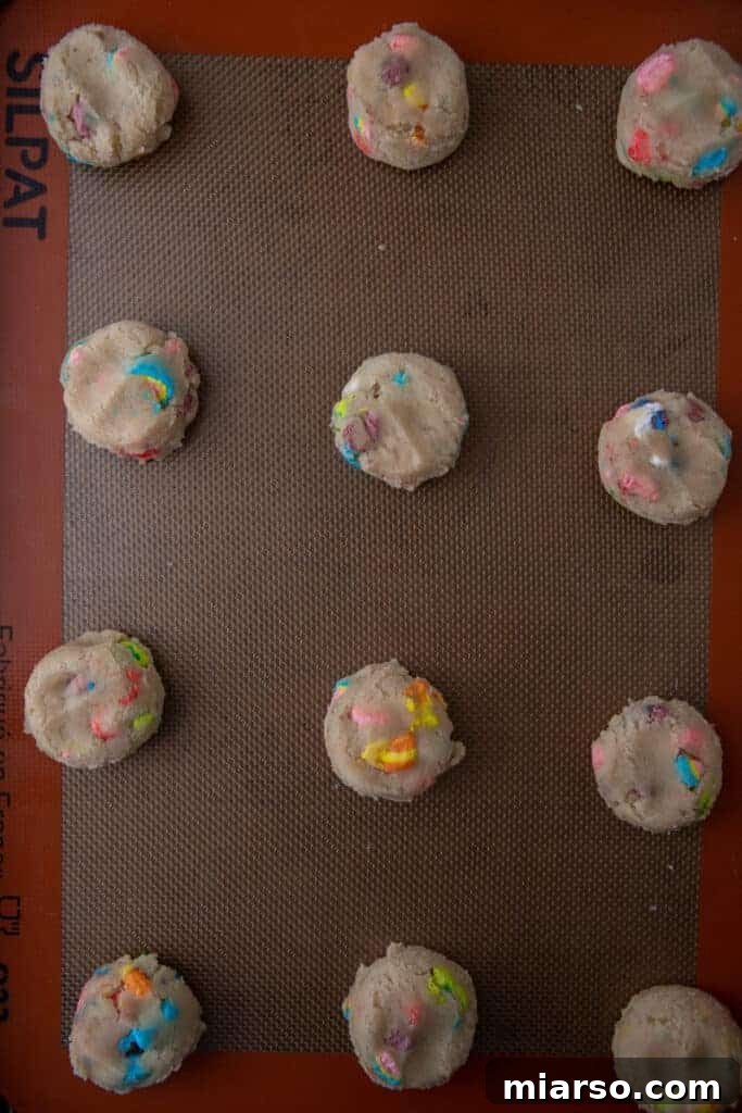 Magical Lucky Charms Cookie Delights 7 Scooped cookie dough balls, coated in marshmallows, on a baking sheet