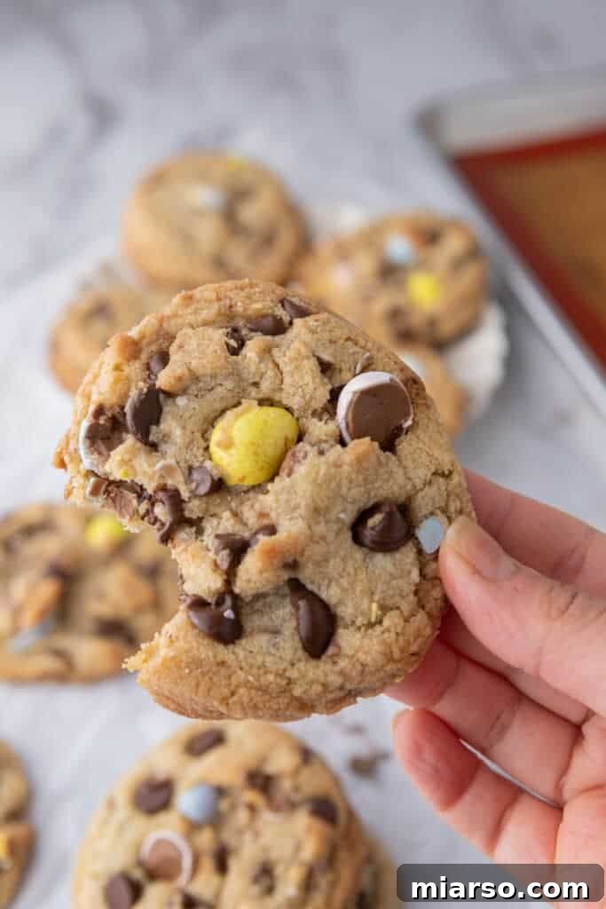 a hand holding up a cadbury egg cookie with a bite taken out