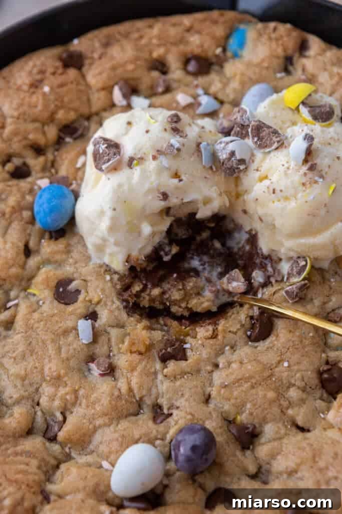 Gooey Giant Cadbury Mini Egg Skillet Cookie 11 A fork taking a bite of Cadbury Mini Egg Skillet Cookie, showing its gooey center and melted ice cream.