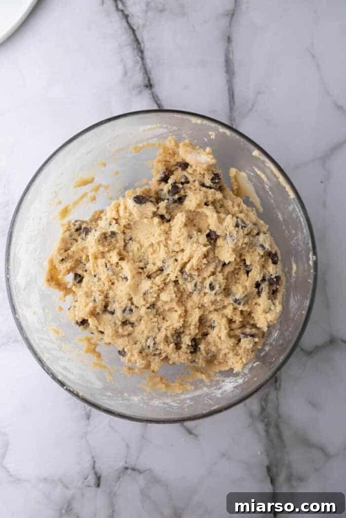 The fully mixed chocolate chip cookie dough, rich and dense, resting in a bowl, ready to be spread into the baking pan.