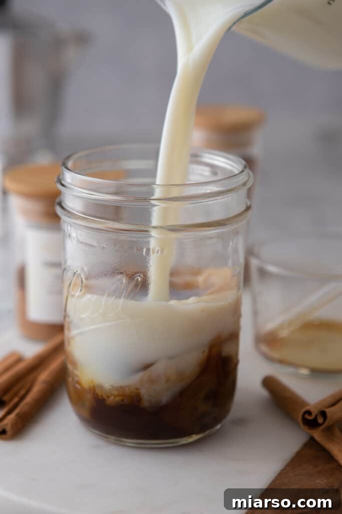 Fresh milk being poured over ice and espresso in a glass, creating a beautiful layered effect for an iced latte.