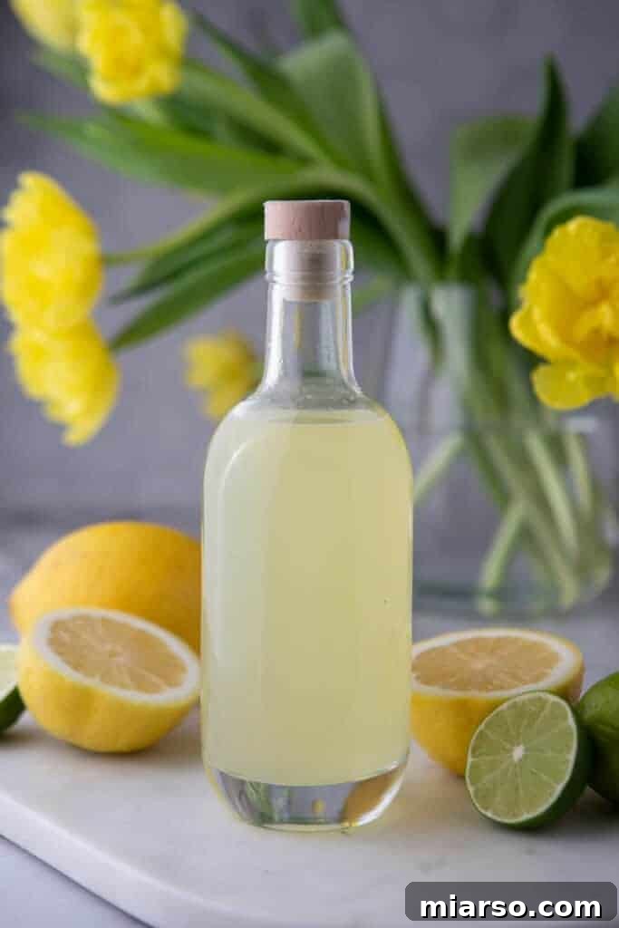 Bottle of homemade lemon sour mix on a wooden table, with cocktail glasses nearby
