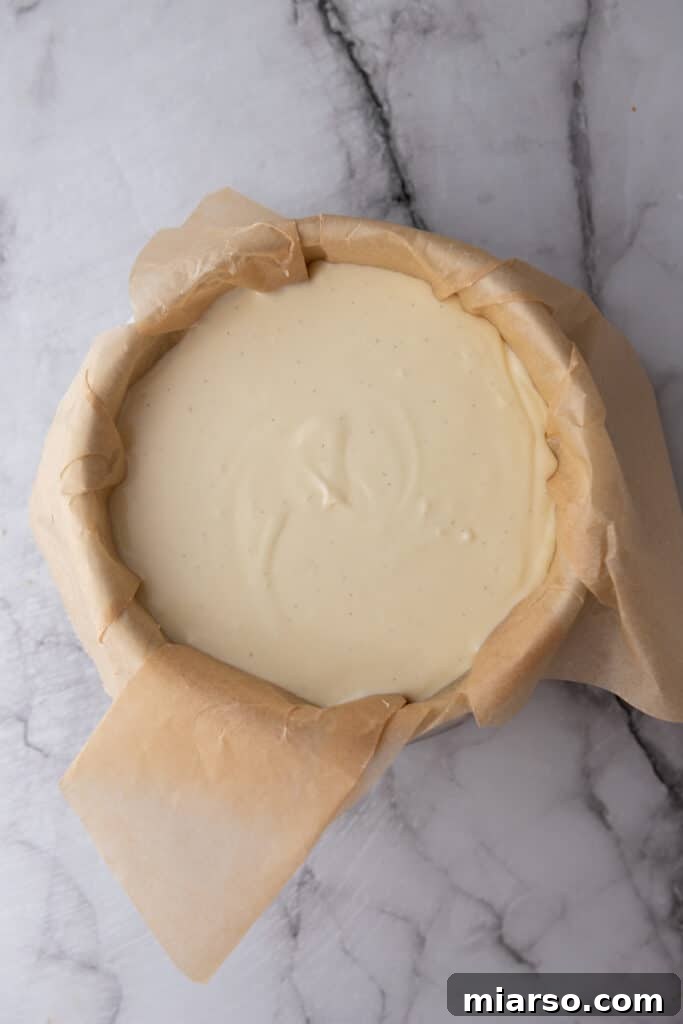Raw cheesecake batter poured into a parchment-lined springform pan