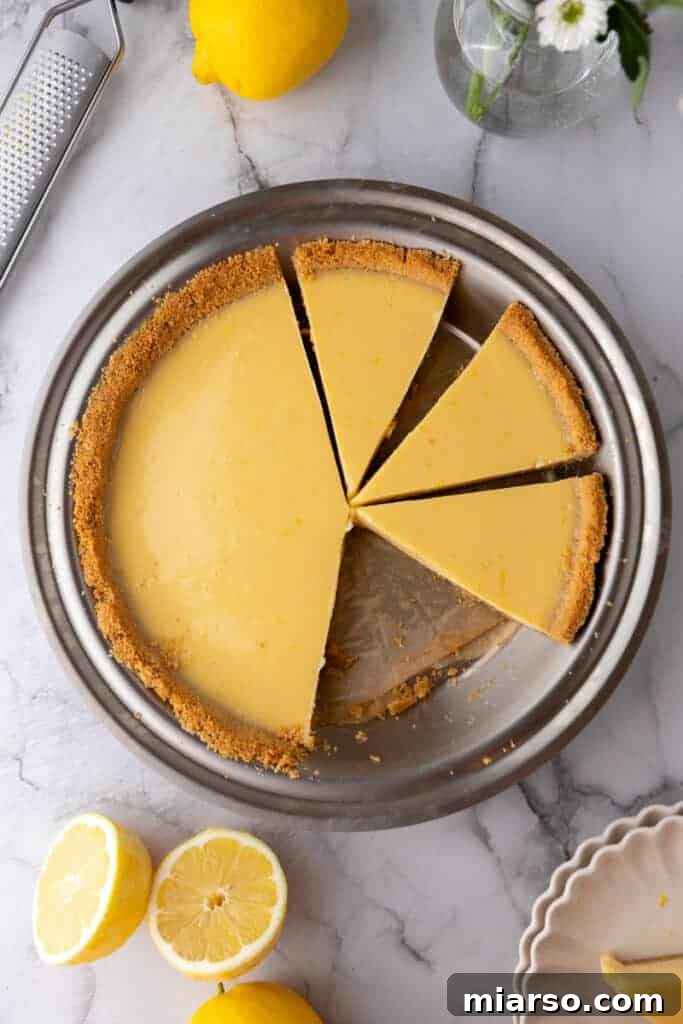A beautifully set lemon pie with a golden graham cracker crust, garnished with fresh lemon slices and a dollop of whipped cream, in a pie pan