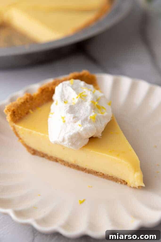 A perfect slice of lemon pie with graham cracker crust and whipped cream on a white plate, ready to be enjoyed