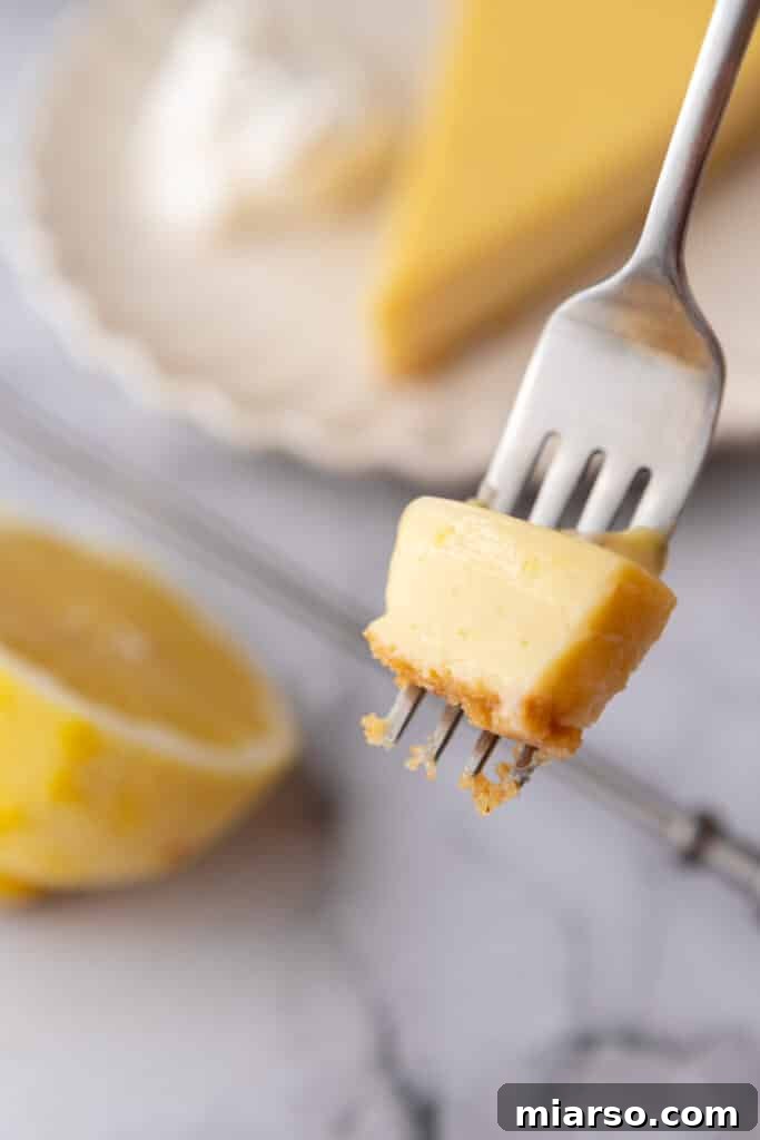 A fork taking a perfect bite out of a slice of lemon pie, showing the layers of graham cracker crust, creamy lemon filling, and fluffy whipped cream