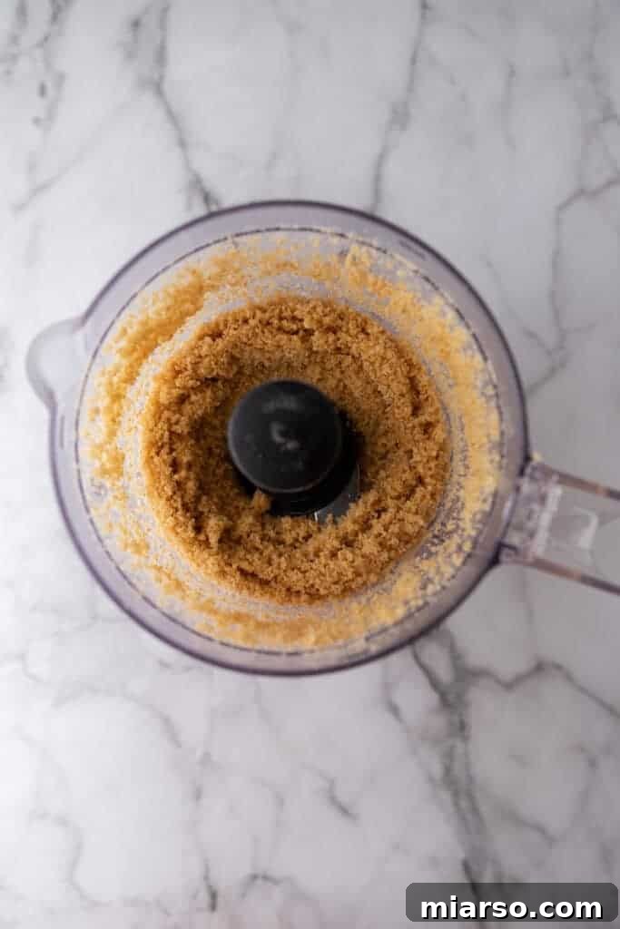 Graham cracker crumbs being processed in a food processor, creating a fine, uniform texture