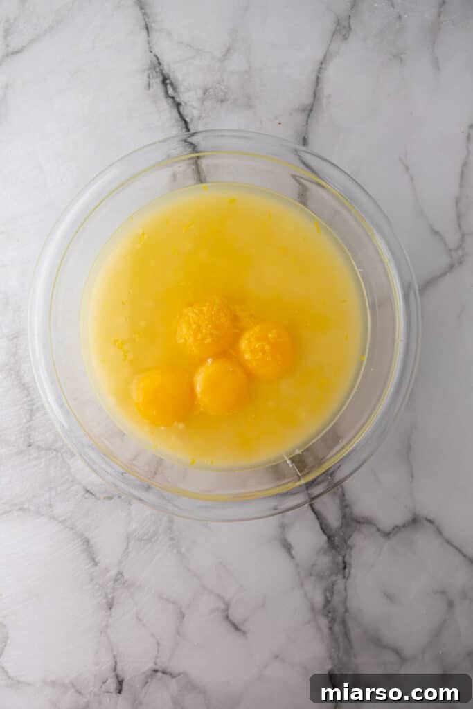 Unmixed wet and dry ingredients for the lemon pie filling (condensed milk, egg yolks, lemon juice, lemon zest) in a large glass bowl